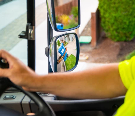 A man driving a food waste pickup truck and looking container in rear mirror